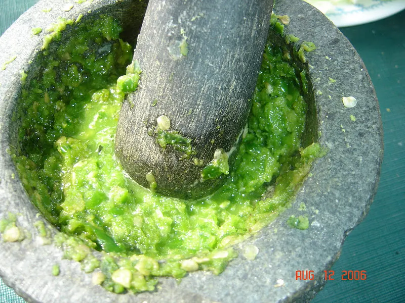 Crushing fresh green chilies with a mortar and pestle.