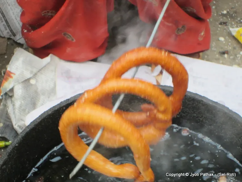 ... removing the fried bread carefully with a thick wooden stick and letting the extra oil drip back in the oil before transferring into a large aluminum bowl.