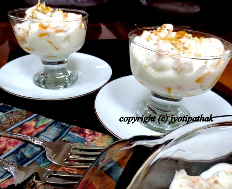 ... making individual desserts cups by spooning mango-sikarni mixture, topped with chopped nuts into parfait glass bowl.