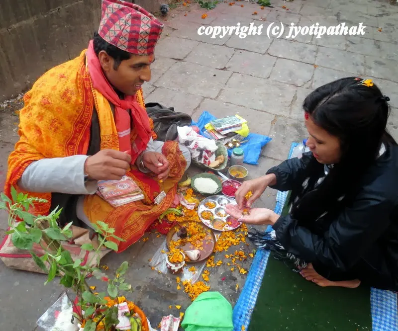 A Brahmin priest is chanting in Sanskrit in the temple area and offering vermillion tikaa and blessing to a devotee.