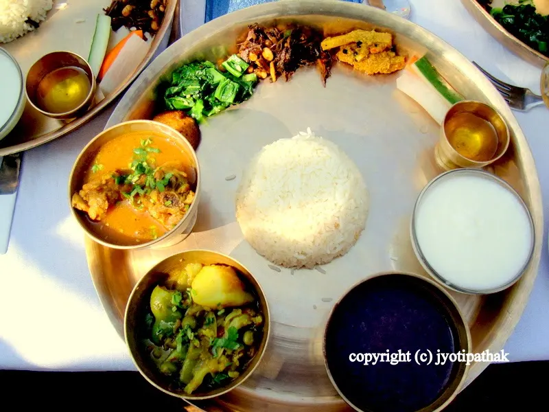 For a taste of an authentic Nepali daal-bhaat-tarkaari, try Thakali food - accompanying dishes are buttered rice in the center, with seasonal vegetables, chicken curry, black daal, achaar dish, and a bowl of yogurt.